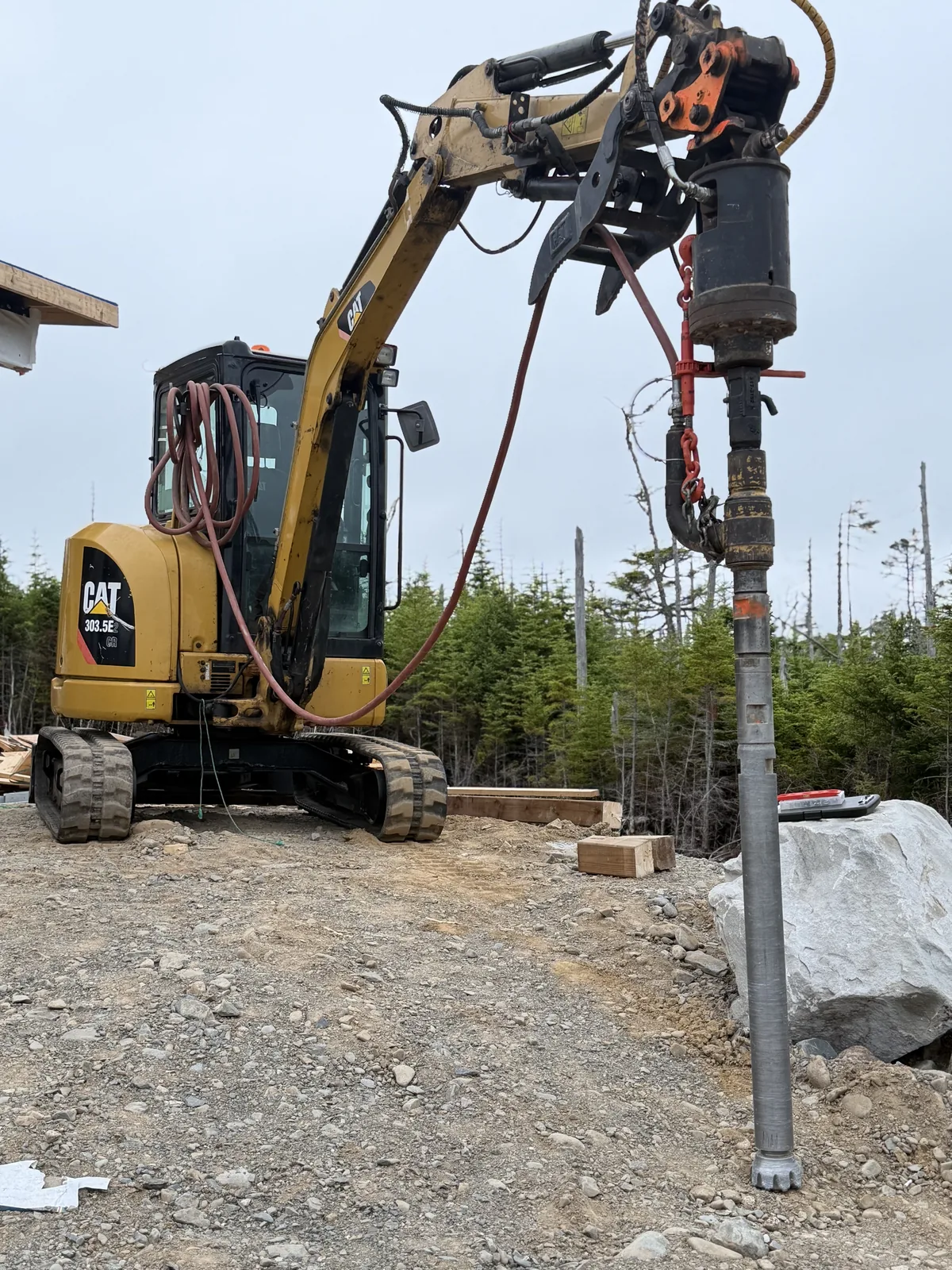 High-torque rock drilling rig anchoring a pile beside a granite boulder