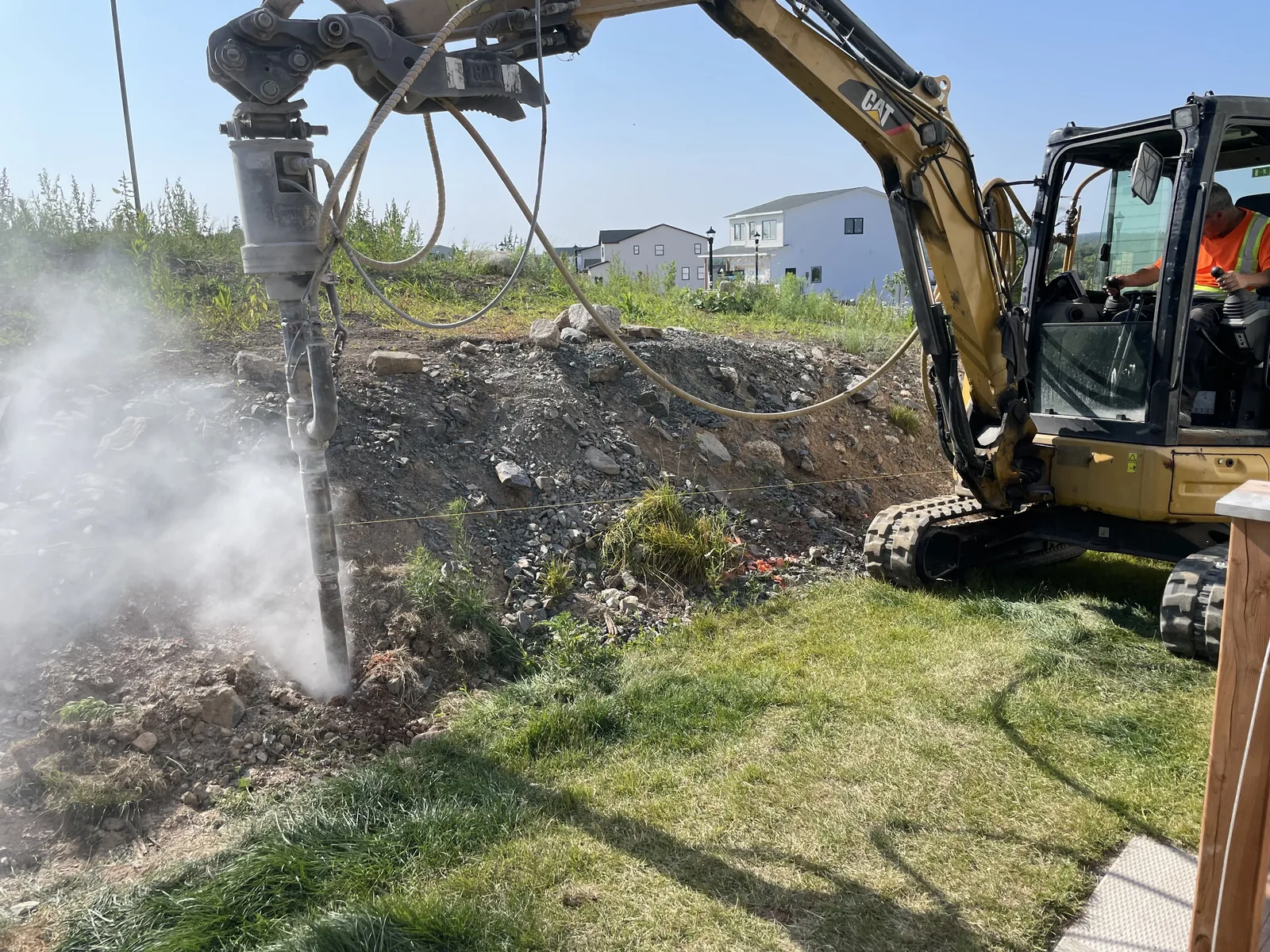 Rock drilling rig with driver, dust cloud, new subdivision build